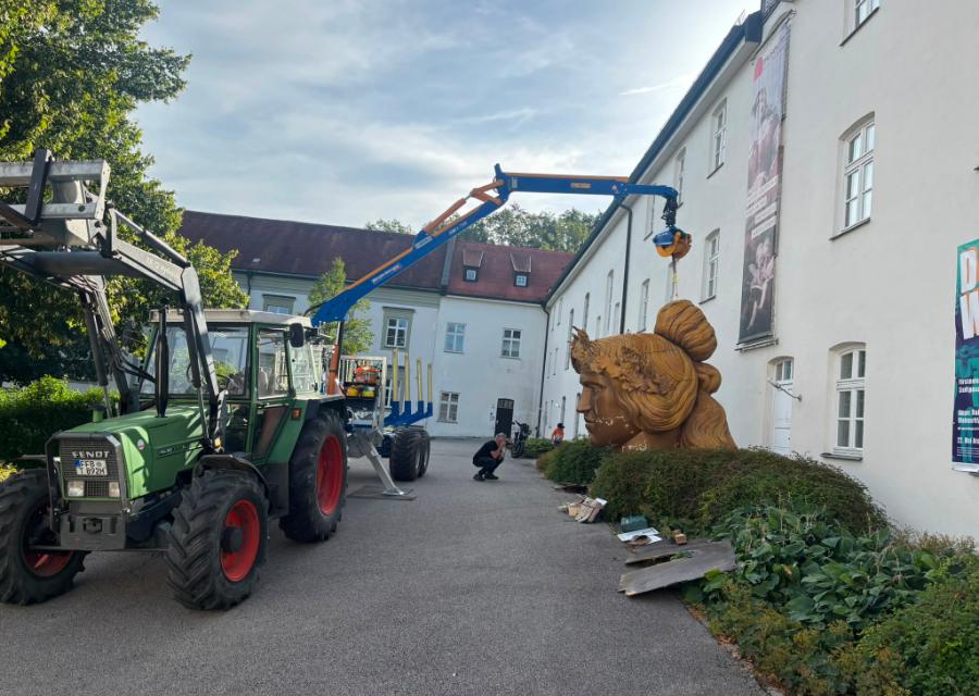 Traktor mit Ladekran vor dem Museum Fürstenfeldbruck, daneben der über drei Meter hohe Kopf der Bavaria